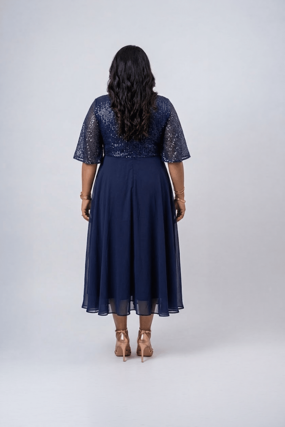 Woman wearing a midnight navy sequin gown with a wrap V-neckline, elbow-length sleeves and a flowing A-line skirt