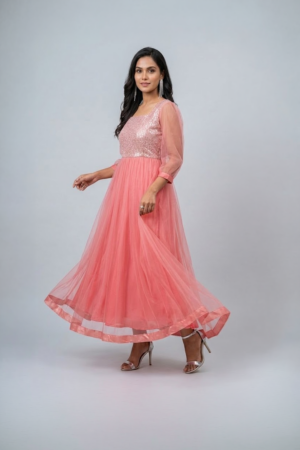 Woman wearing a coral pink shimmering tulle gown with a sequin bodice, square neckline and sheer three-quarter sleeves