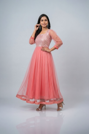 Woman wearing a coral pink shimmering tulle gown with a sequin bodice, square neckline and sheer three-quarter sleeves