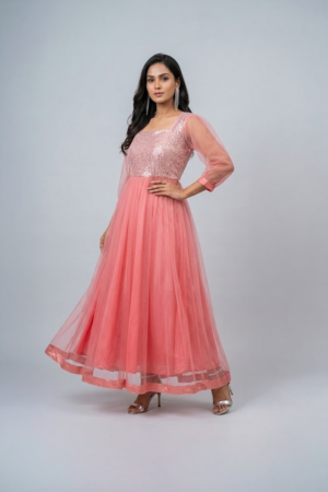 Woman wearing a coral pink shimmering tulle gown with a sequin bodice, square neckline and sheer three-quarter sleeves