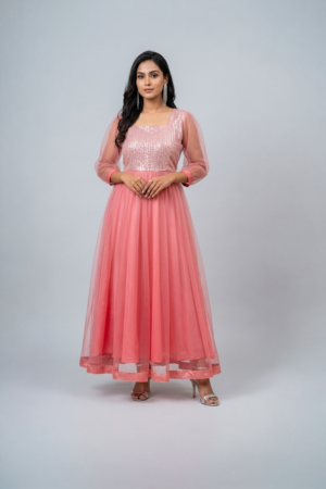 Woman wearing a coral pink shimmering tulle gown with a sequin bodice, square neckline and sheer three-quarter sleeves