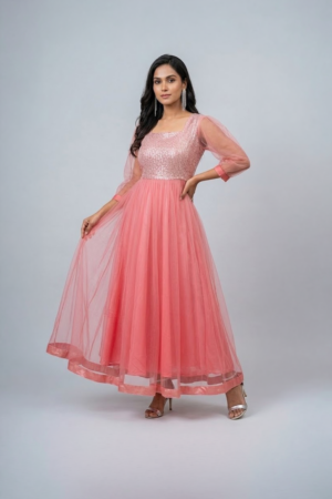 Woman wearing a coral pink shimmering tulle gown with a sequin bodice, square neckline and sheer three-quarter sleeves