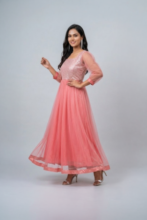 Woman wearing a coral pink shimmering tulle gown with a sequin bodice, square neckline and sheer three-quarter sleeves