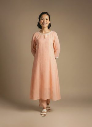“Woman wearing a peach-orange embroidered kurta set with round neckline, keyhole detail, and matching pants, standing barefoot against a beige background.”
