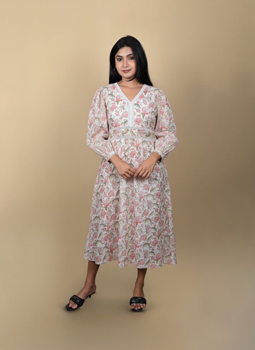 "Full view of a woman wearing a white and pink floral midi dress with long sleeves and lace detailing, posing against a beige background"