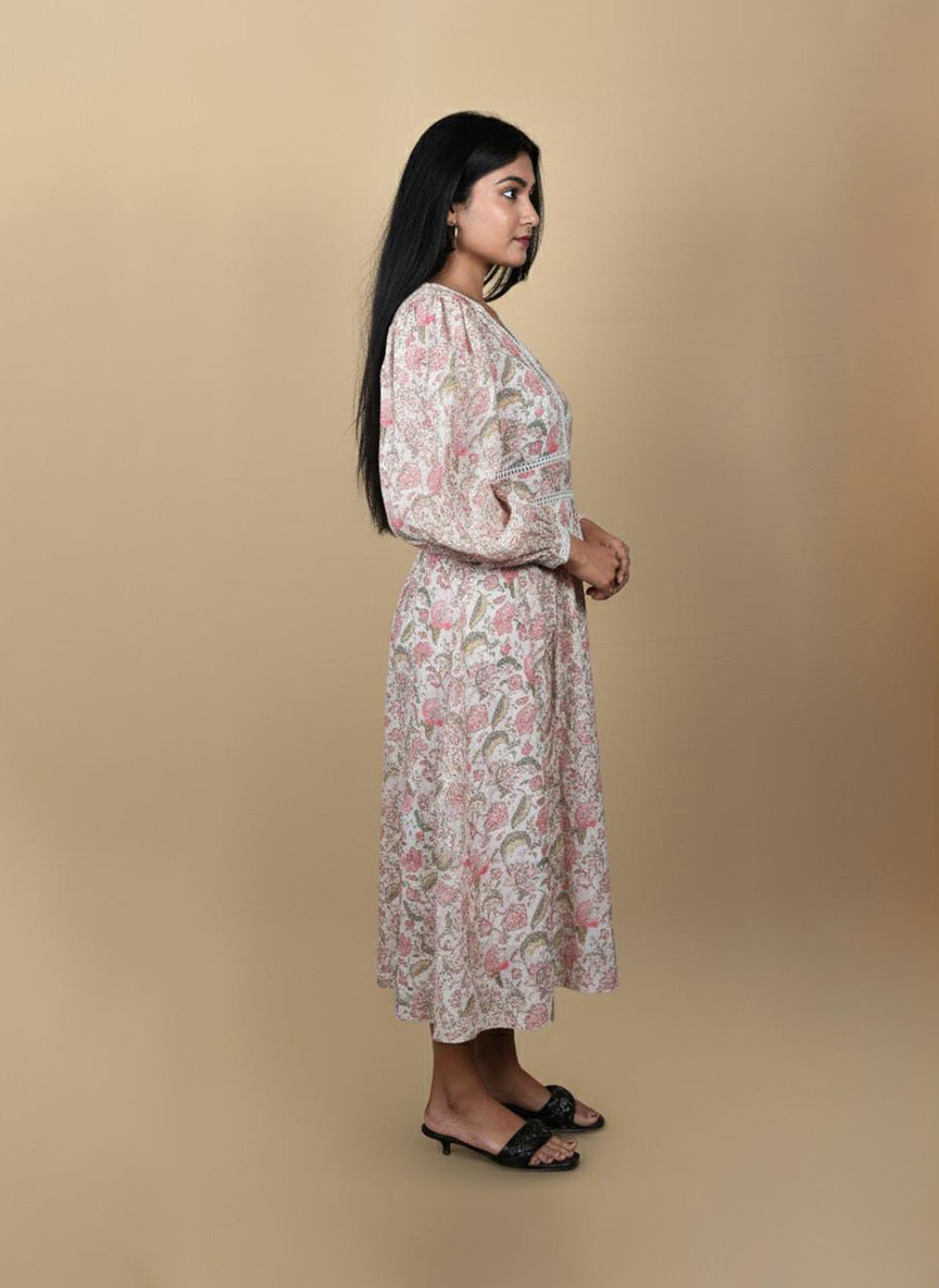 "Full view of a woman wearing a white and pink floral midi dress with long sleeves and lace detailing, posing against a beige background"