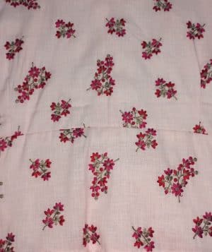 “Woman wearing a sleeveless pink cotton floral midi dress with a gathered waist and tiered hem, standing against a beige background.”