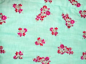 “Woman wearing an aqua green floral cotton midi dress with wide shoulder straps and pink flower prints, standing against a beige background.”