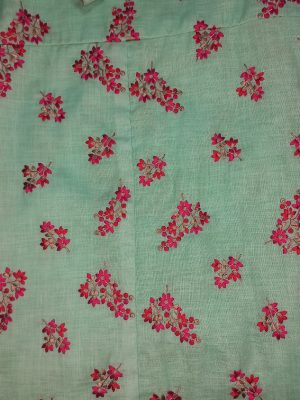 “Woman wearing an aqua green floral cotton midi dress with wide shoulder straps and pink flower prints, standing against a beige background.”