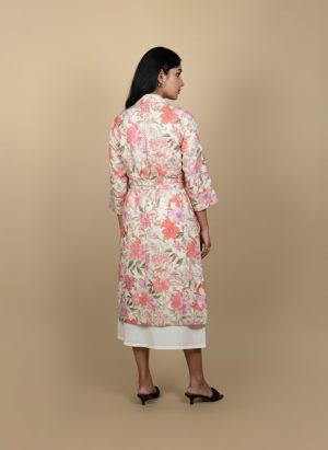 "Full view of a woman wearing a floral printed tie-waist long shrug layered over a white midi dress, posing against a beige background"
