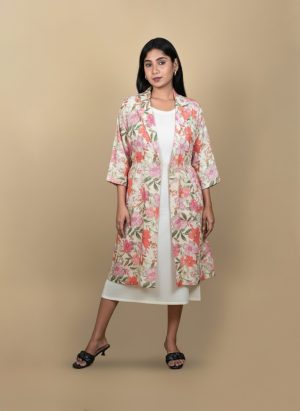 "Full view of a woman wearing a floral printed tie-waist long shrug layered over a white midi dress, posing against a beige background"