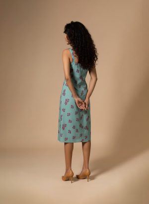 “Woman wearing an aqua green floral cotton midi dress with wide shoulder straps and pink flower prints, standing against a beige background.”
