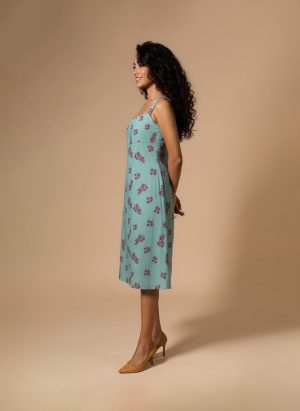 “Woman wearing an aqua green floral cotton midi dress with wide shoulder straps and pink flower prints, standing against a beige background.”