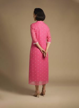 “Woman wearing a pink chikankari cotton kurta dress with white floral embroidery, V-notch neckline, and 3/4 sleeves standing against a beige background.”