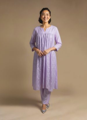 Woman standing and smiling, wearing a light lavender kurta with subtle patterns and matching pants.