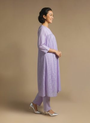 Woman standing and smiling, wearing a light lavender kurta with subtle patterns and matching pants.