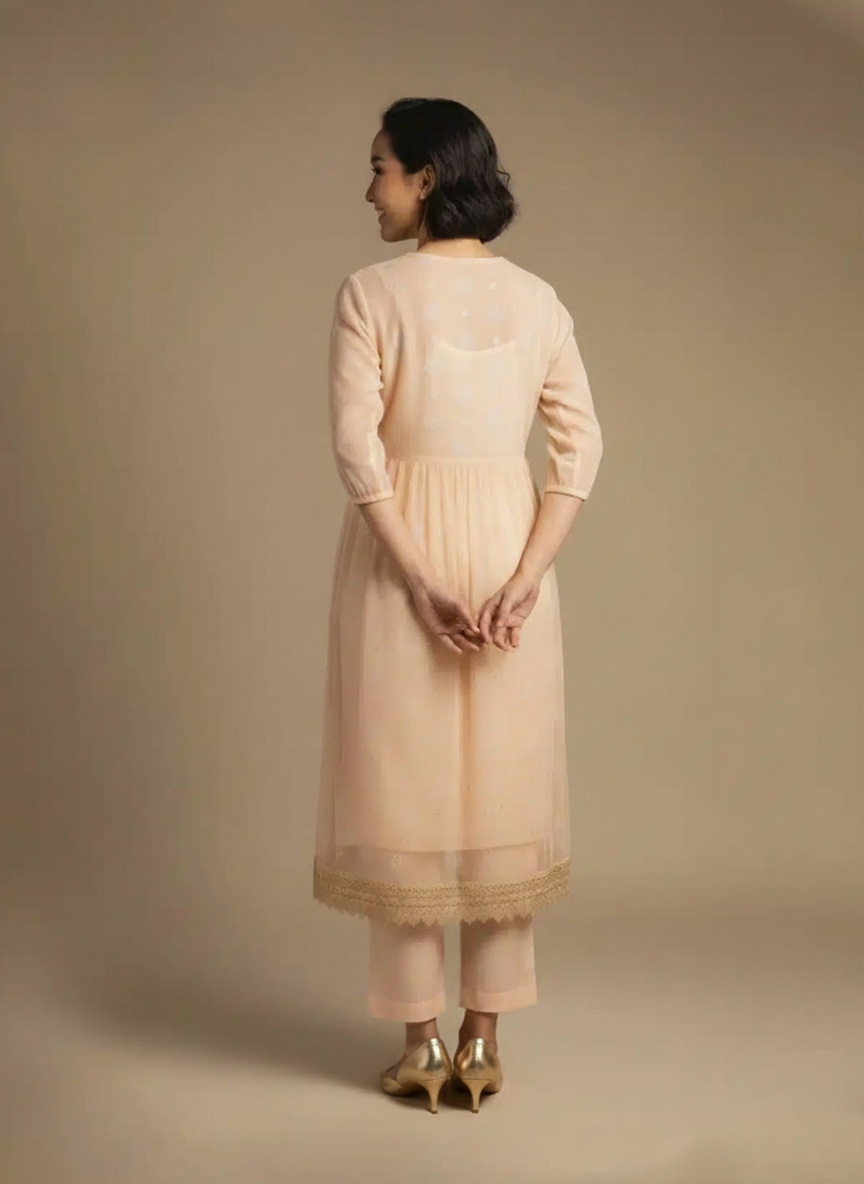 “Woman wearing a peach Kota embroidered kurta set with gold lace border and sheer full sleeves, standing against a beige background.”