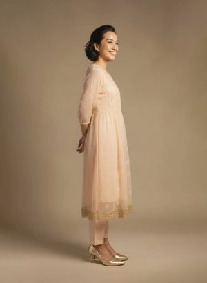 “Woman wearing a peach Kota embroidered kurta set with gold lace border and sheer full sleeves, standing against a beige background.”