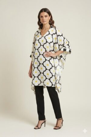 Woman wearing a black and white oversized floral printed tunic with yellow accents, featuring a relaxed silhouette and V-neckline, paired with slim black trousers and heels.