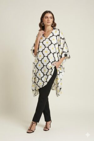 Woman wearing a black and white oversized floral printed tunic with yellow accents, featuring a relaxed silhouette and V-neckline, paired with slim black trousers and heels.