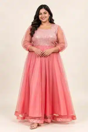 Plus-size model in coral pink shimmering tulle gown, full-length front view showing sequin bodice and sheer sleeves