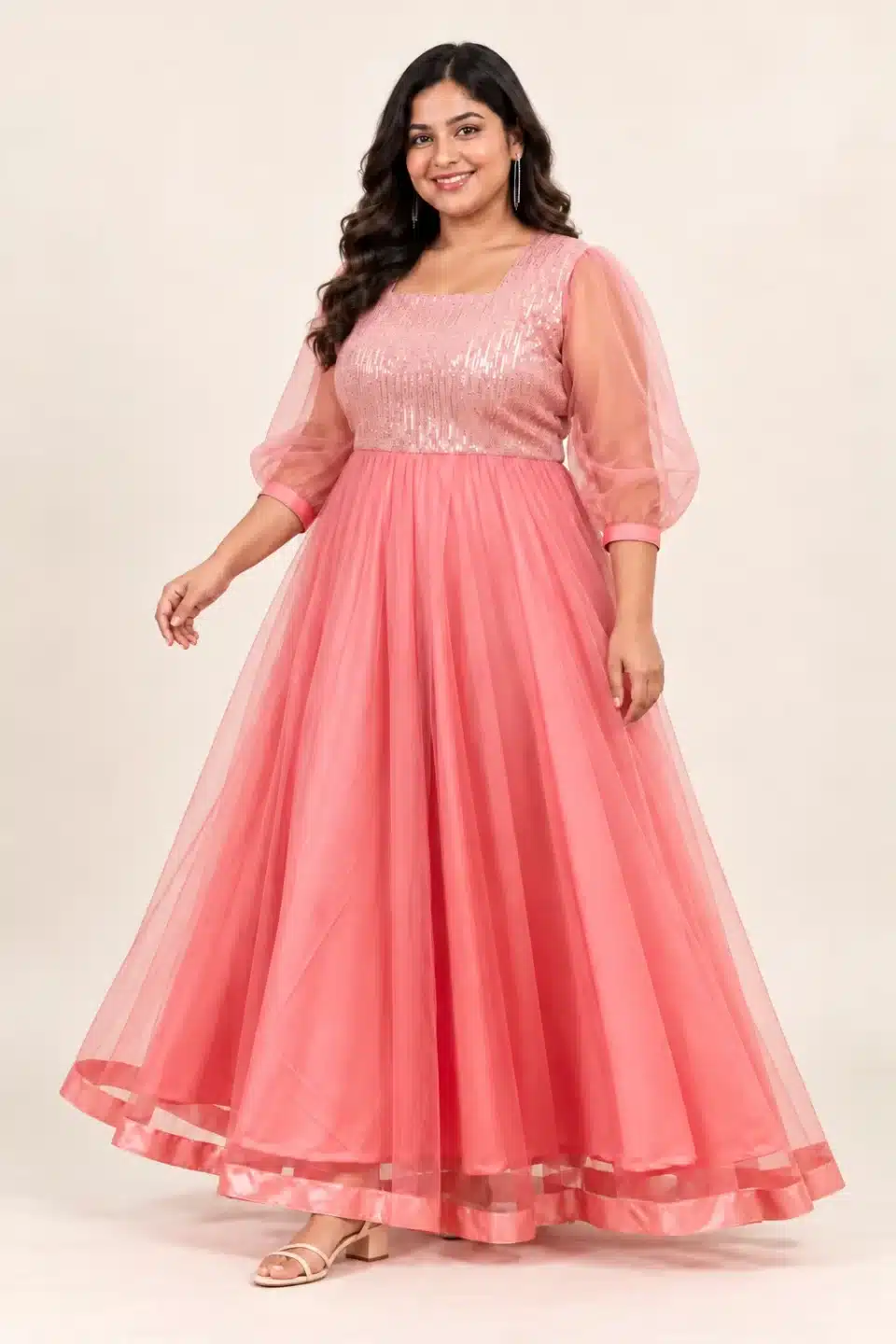 Plus-size model wearing coral pink shimmering tulle gown in a three-quarter pose